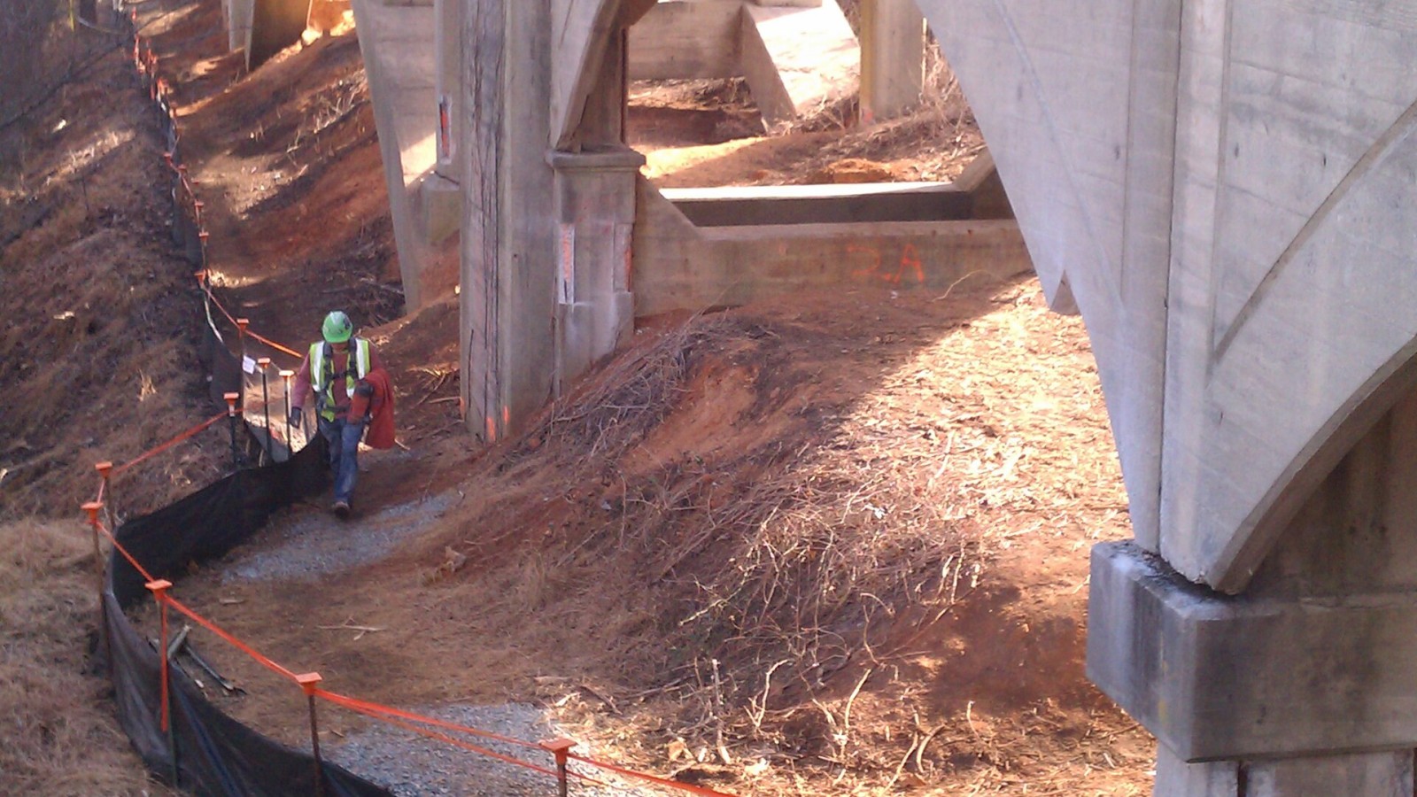 A construction worker walks alongside the aging Wil-Cox Bridge, known for its unique arched architecture. The black tarps were installed along the banks of the Yadkin River to control erosion and prevent repair work curr