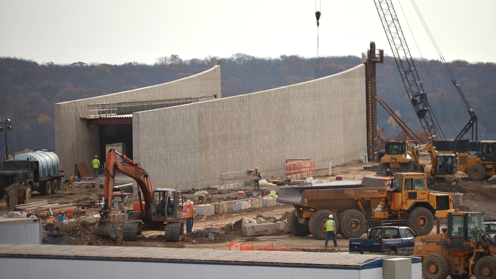Tall concrete walls of the Visitor Center under construction. Surrounded by active construction equipment and workers The main walls of the Visitor Center continue to rise. The sections being poured are on the far side o