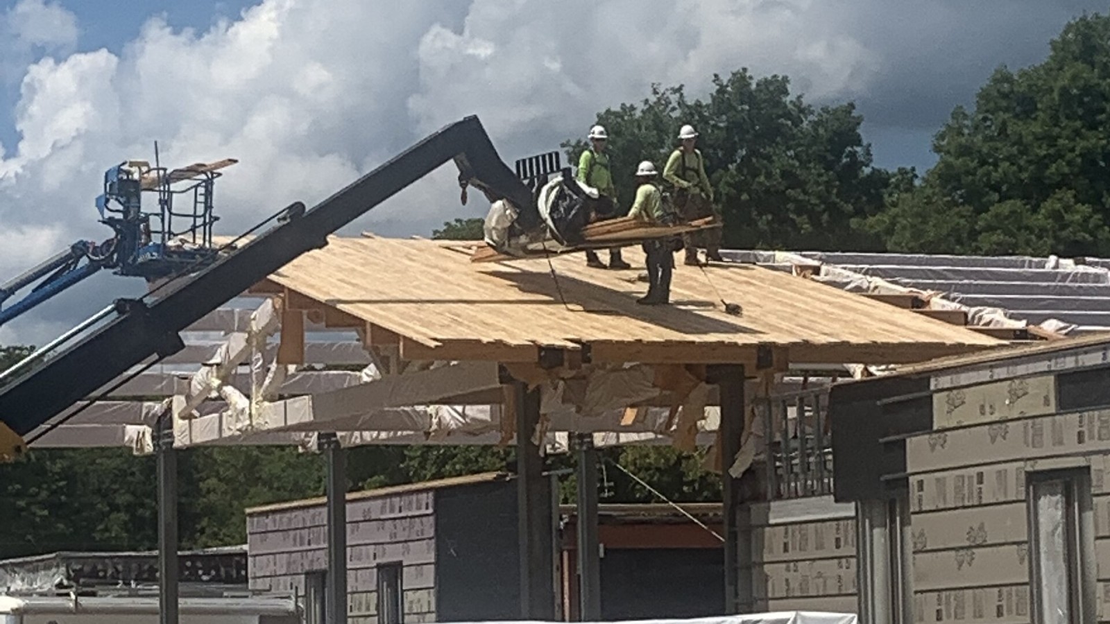 Three construction workers wearing hard hats stand on top of a pitched wooden room. The new pitched roof will create a visual point of interest for visitors entering the main hotel building at Mammoth Cave. Keywords: Gre