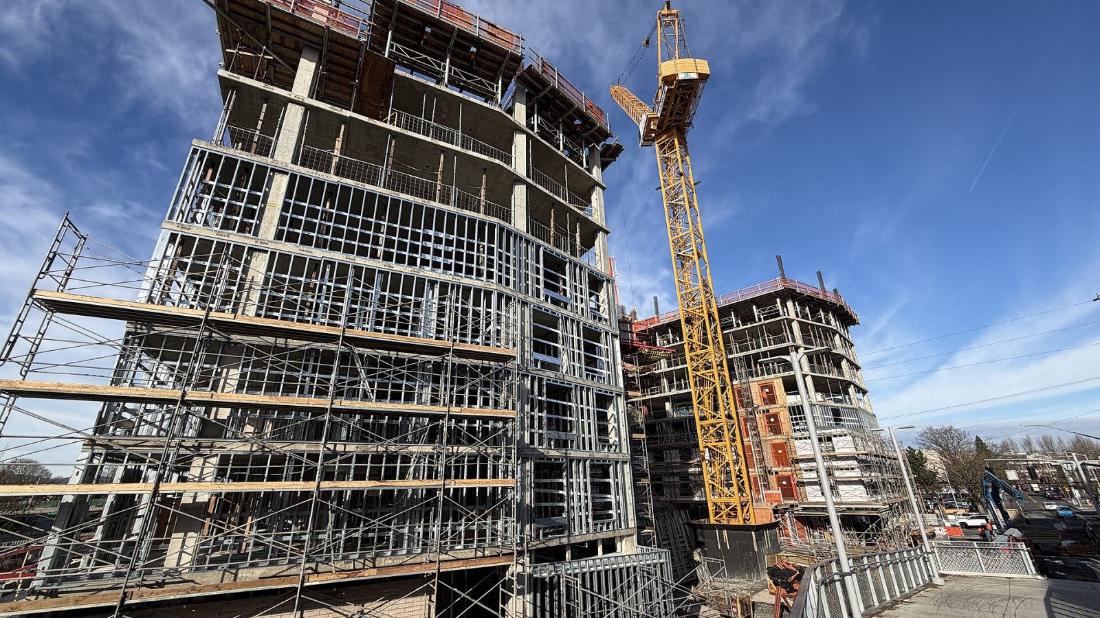 Wide view from public right-of-way of the curved facade and scaffolding of the 12-story hollywoodHUB affordable housing project at Hollywood Transit Center, including the tower crane and adjacent structures.