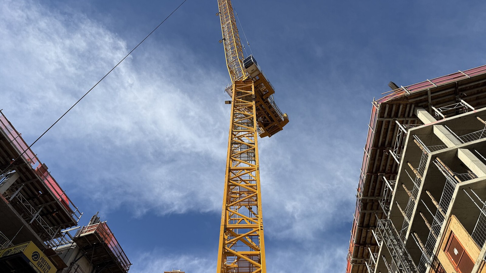 A low-angle view of the yellow tower crane against the blue sky, framed by the emerging concrete and steel structure of the hollywoodHUB project. This 222-unit affordable housing development is located at the Hollywood T