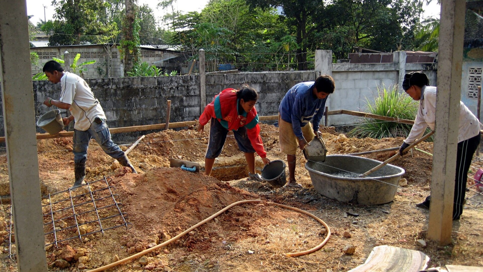 A team of workers mixing concrete in a tub and pouring it with buckets. Location Trat Province, Thailand.