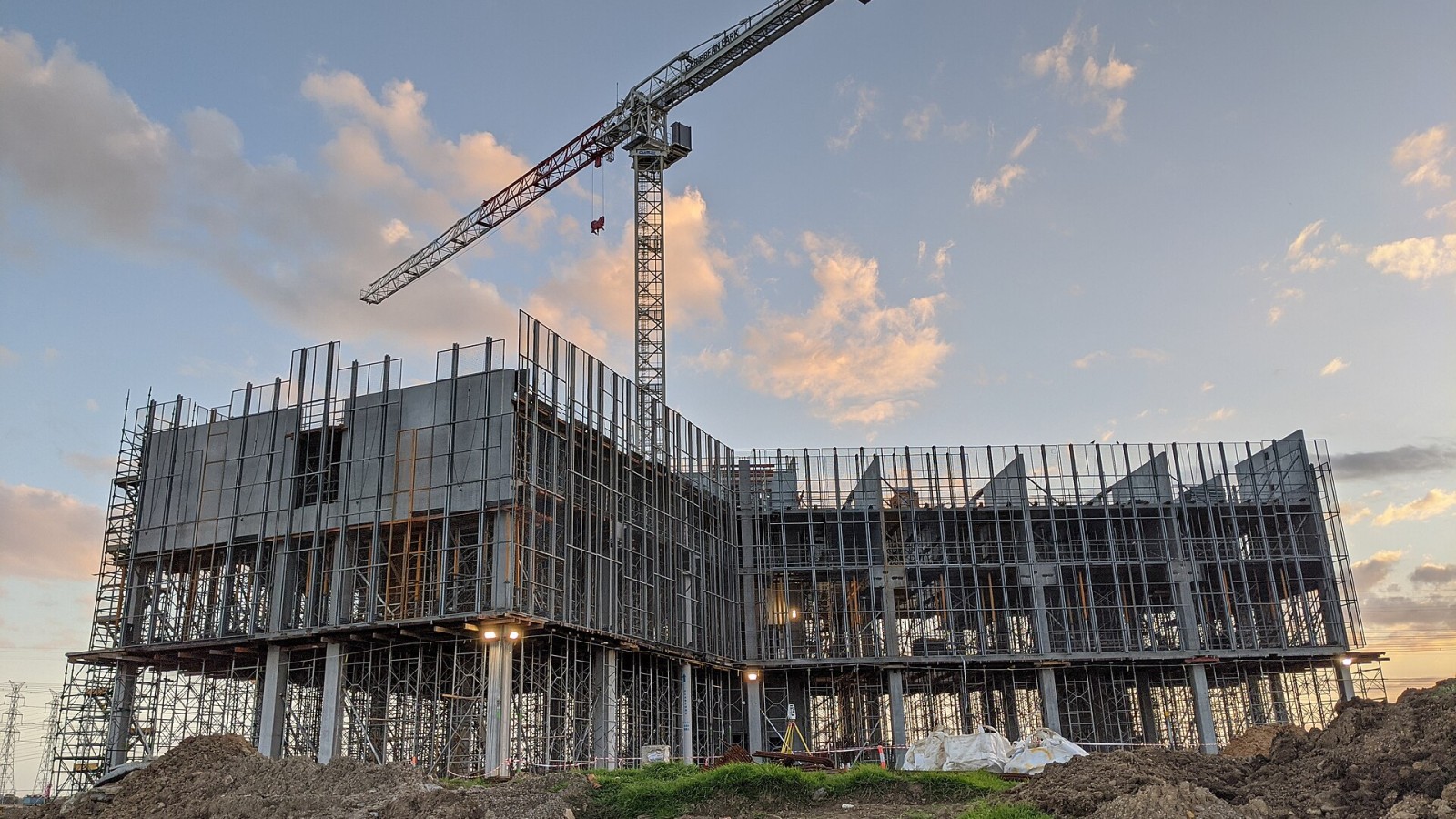 A multistorey concrete building and tower crane at sunset, with survey equipment positioned in front of the active construction site. Photograph by HR Surveyors.