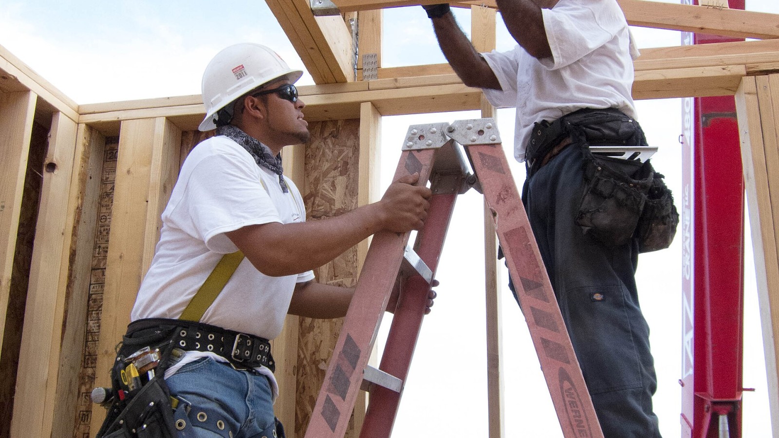 Residential construction workers use a ladder with fall arrest equipment