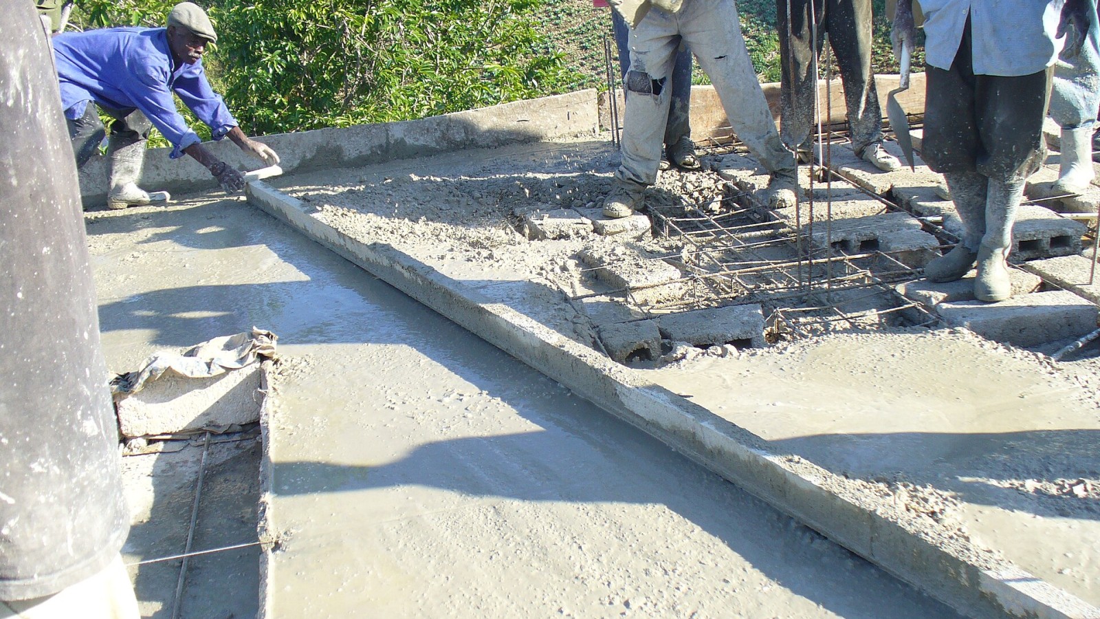 Workers use plank to smooth hand-poured cement on roof of community center