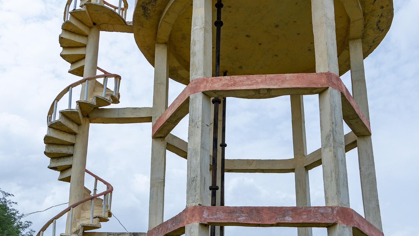Overhead water tank (water tower) in a village in Raichur district, Karnataka, India. The structure consists of a reinforced concrete storage tank elevated on columns, with a spiral staircase for access and maintenance.