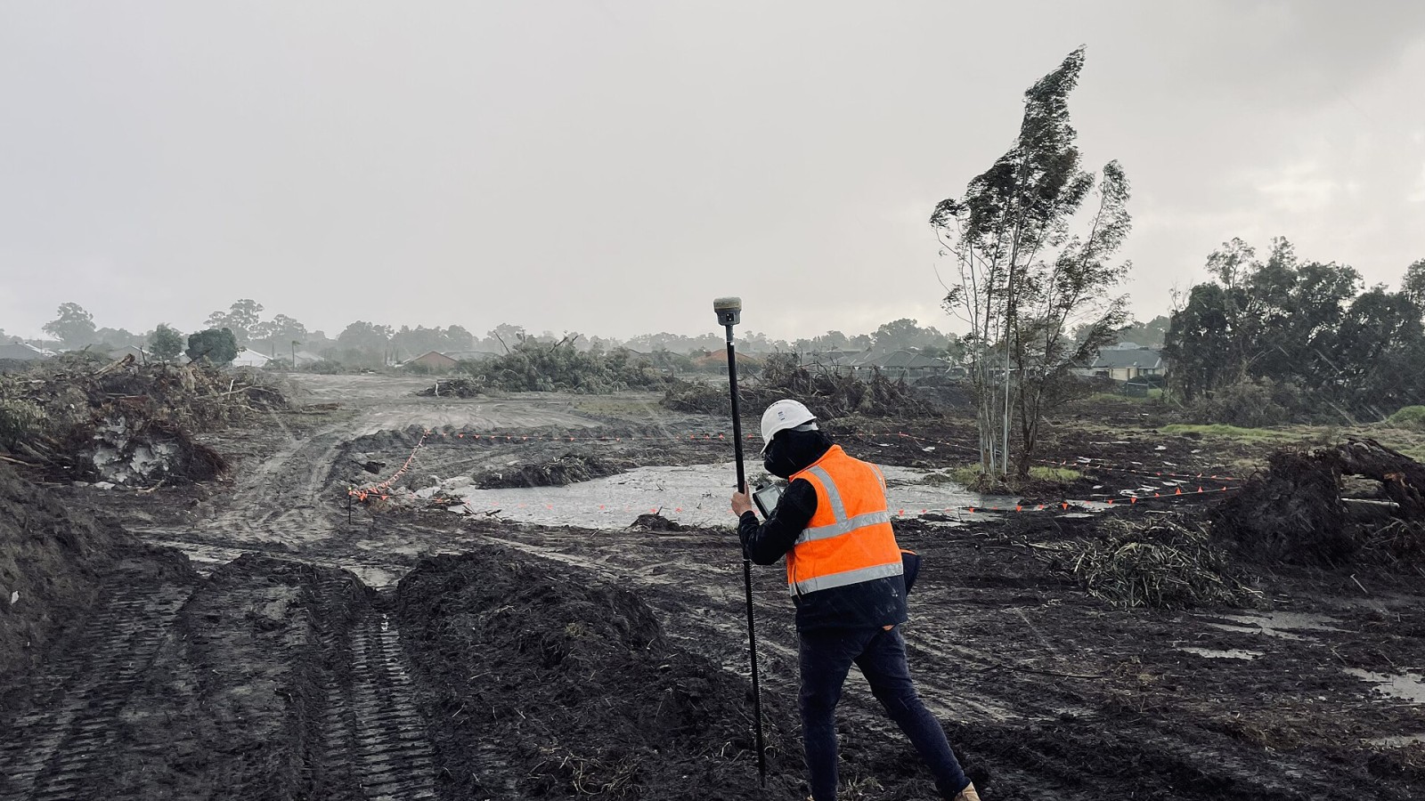 A field surveyor in high-visibility clothing walking across a wet cleared site while collecting measurements with a GNSS receiver. Photograph by HR Surveyors.