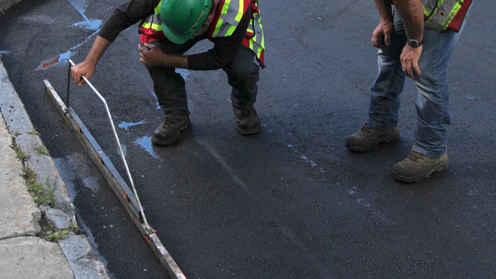 Measurement with a bubble level of the correct slope of a just new asphalt road surface, seen during road construction in Canada