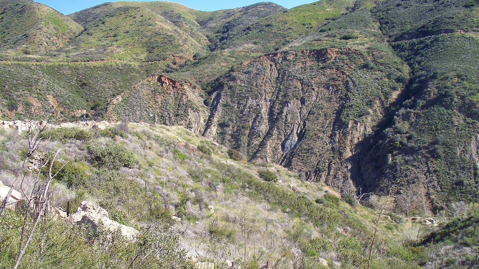 This photo shows the site of the St. Francis Dam in 2009, looking from northwest to southeast across San Francisquito Canyon. The remains of the wing dike made necessary by changes to the height of the dam while under co