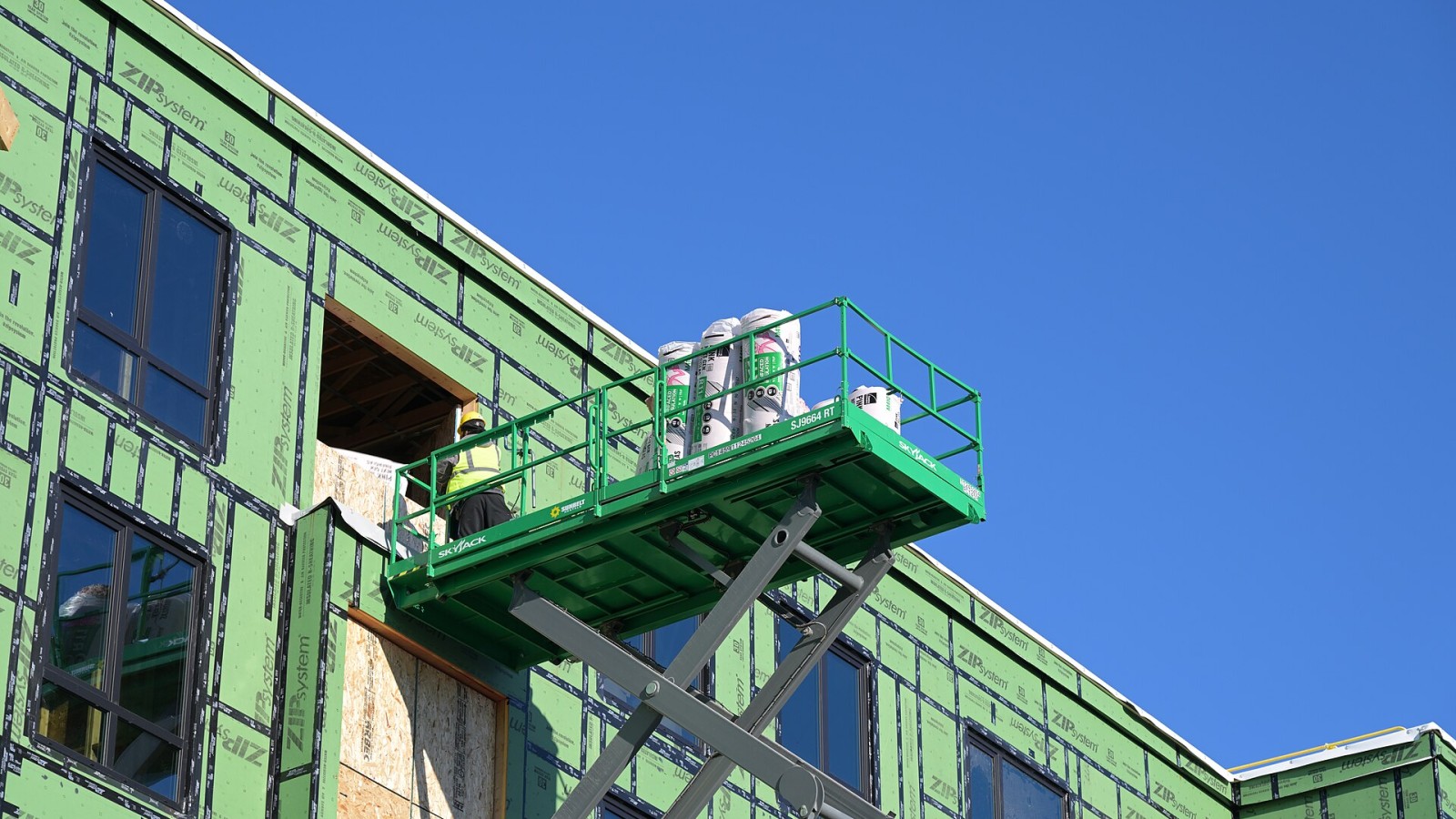 A worker uses a scissor lift to lift rolls of insulation into the top floor at the 53 Pleasant Street construction site in Watertown Square.