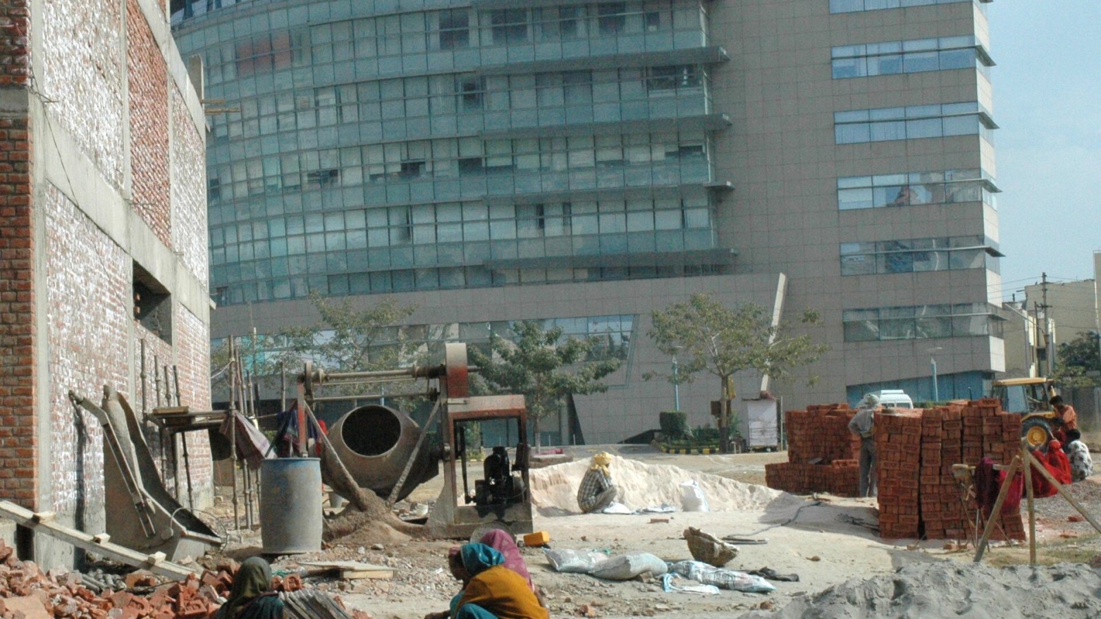 Workers crushing bricks by hand in front of a modern office building, Gurgaon.
