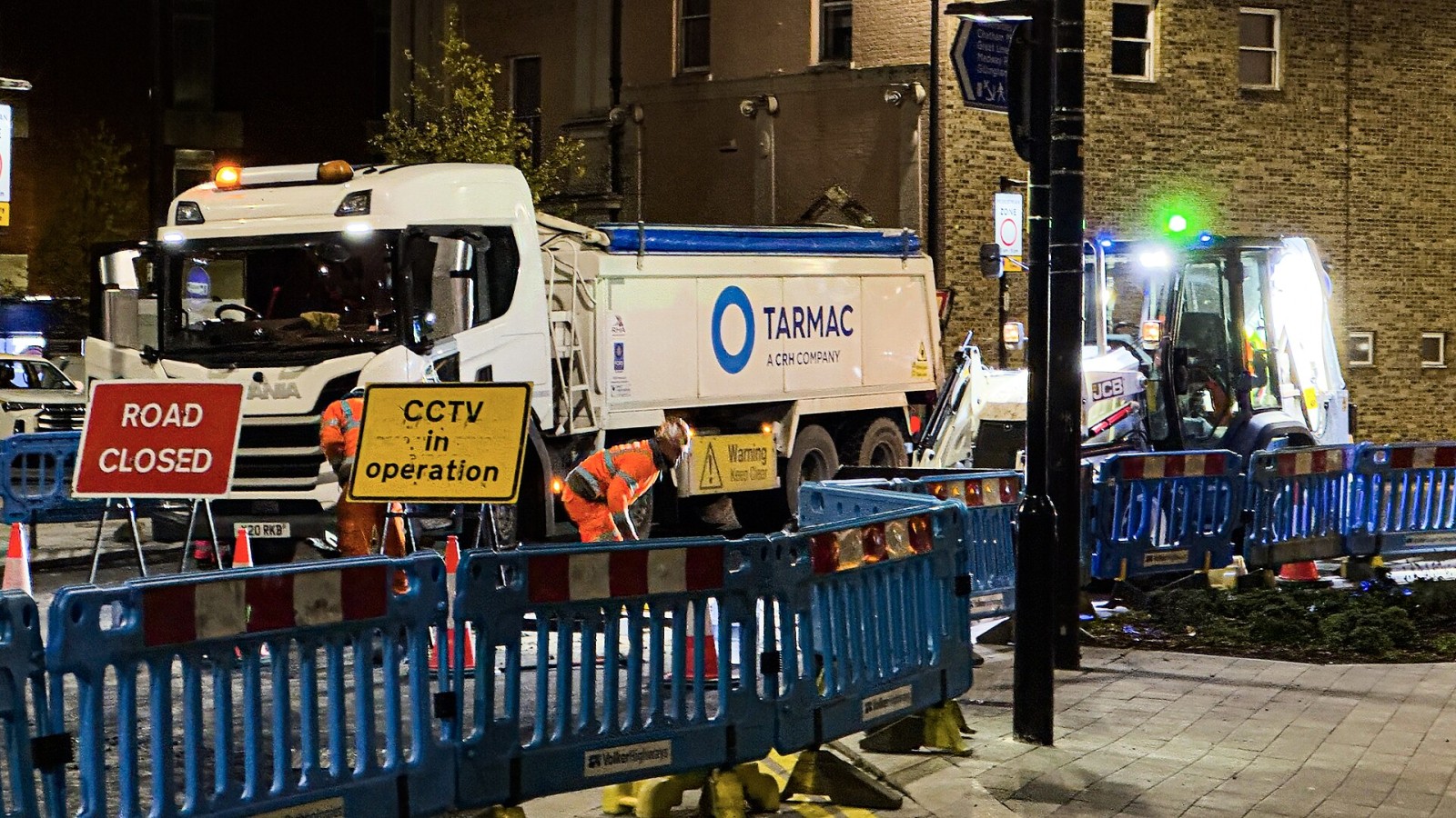 This night time photograph shows road repair work taking place on Globe Lane during improvements to Chatham Waterfront bus station in Chatham, Kent, England, capturing an active construction site with several vehicles an