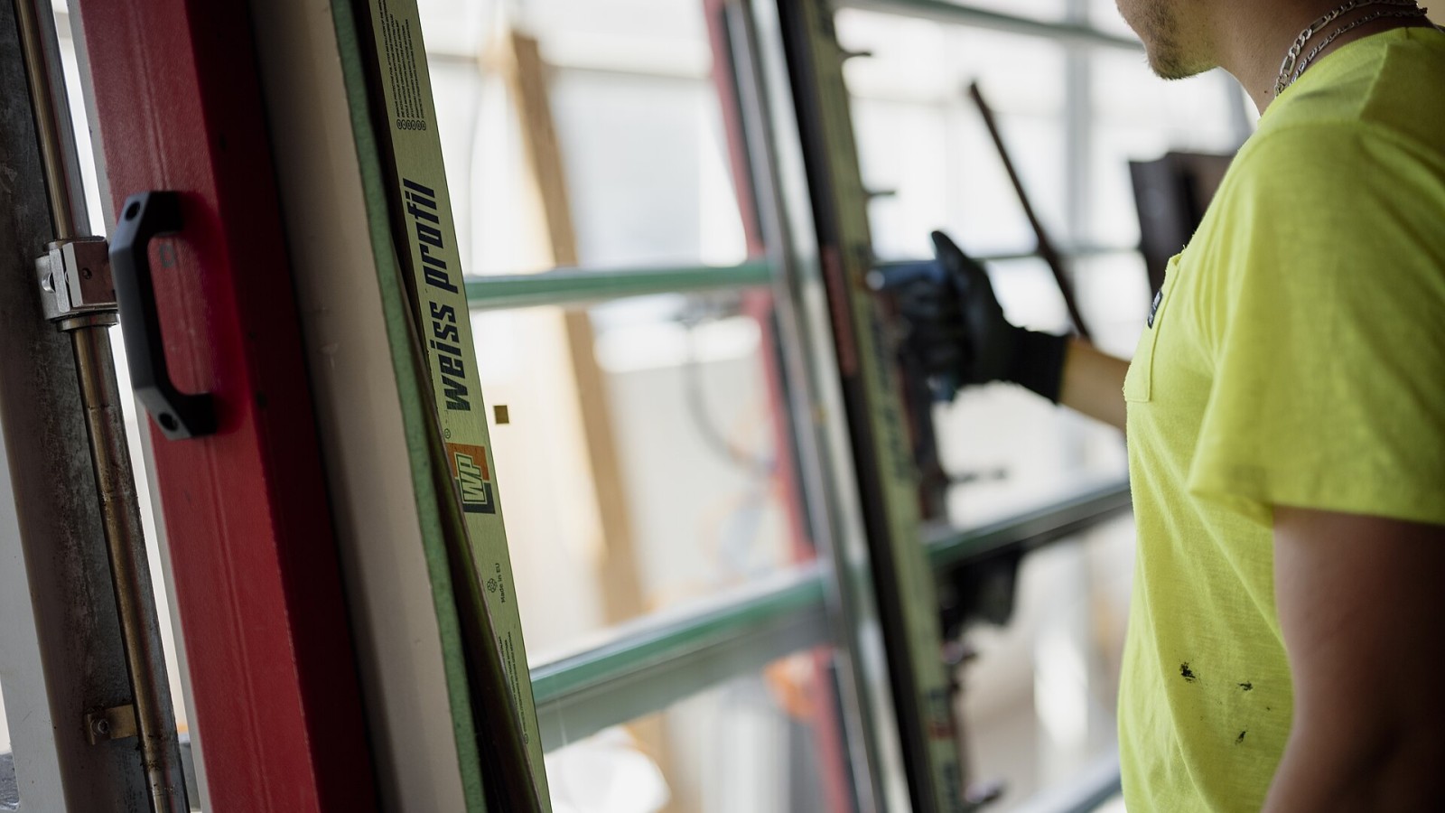 A person is working on installing a window in a construction site. Sunlight is coming through the open space, and tools are visible around.