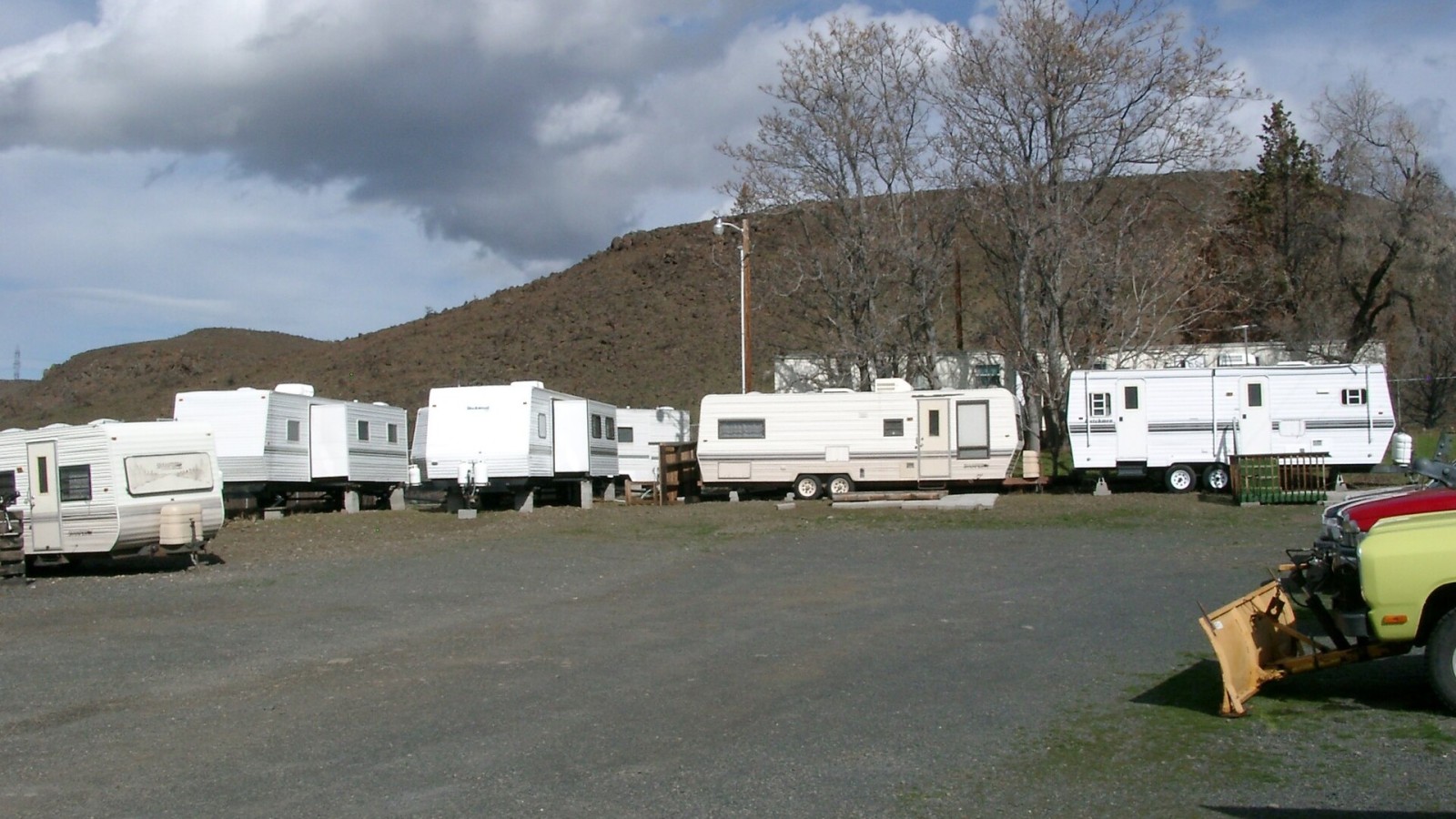 Trailers parked in a parking lot on a cloudy day. The original housing facilities consisted of travel trailers and mobile homes which needed repairs. The original facilities also did not have enough storage or meeting sp