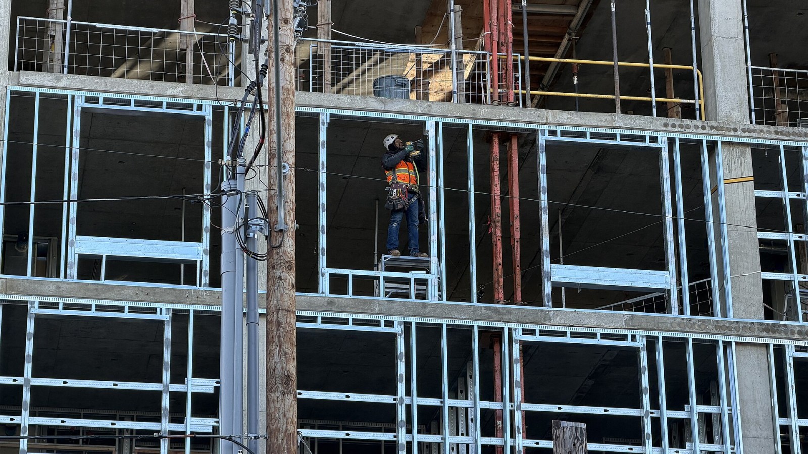 A construction worker in safety gear works on metal stud framing high up in the structural grid of the 12-story hollywoodHUB affordable housing development at the Hollywood Transit Center site. This transit-oriented proj